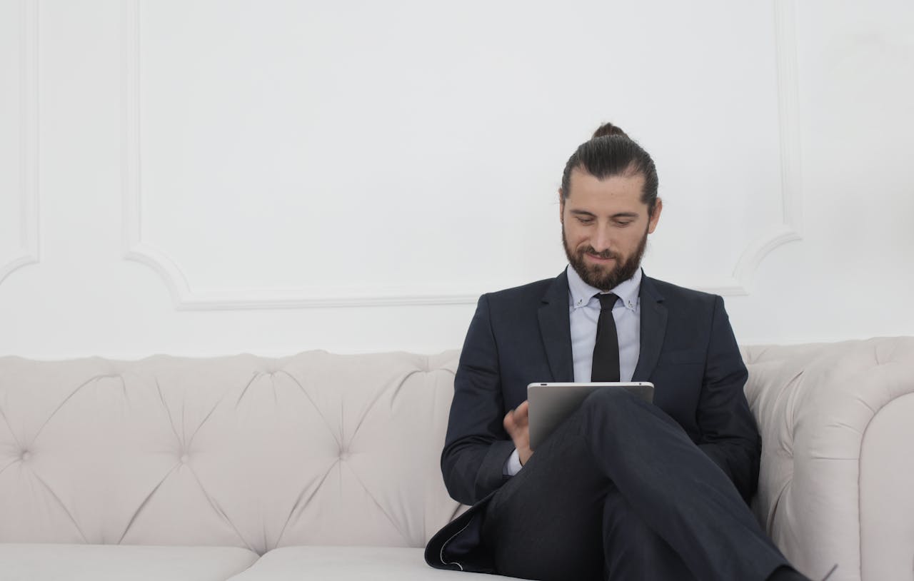 A businessman in a suit sitting on a sofa using a tablet, smiling.